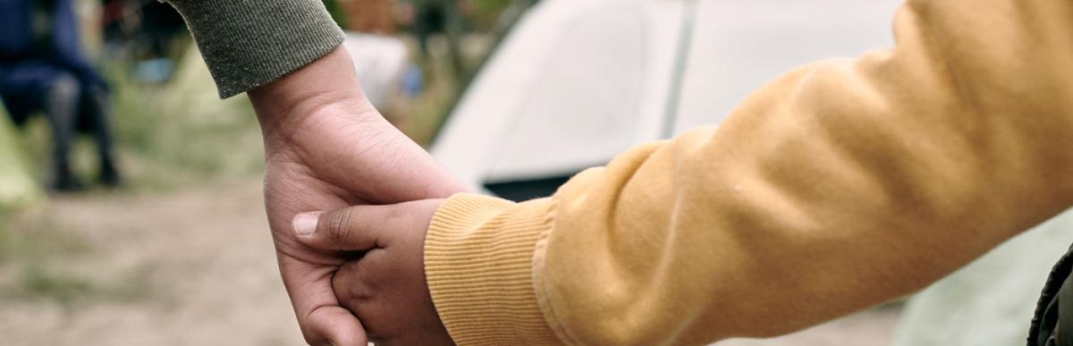 Adult holding child's hand at an encampment