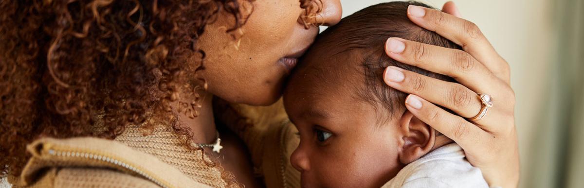 Close-up of a mother kissing her baby boy cradled in her arms at home.