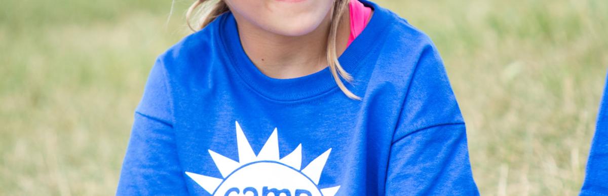 Girl sitting cross legged at summer camp wearing a Camp Kidaca tshirt