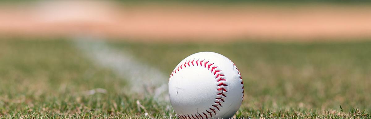 Baseball on foul line with base and outfield out of focus in background.