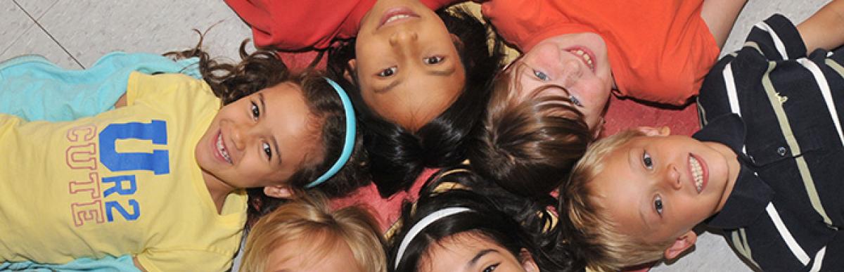 Smiling kids laying on floor in a circle with their heads touching