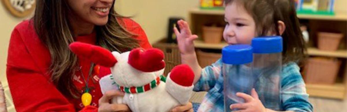 Early child educator showing toy to young child in playroom
