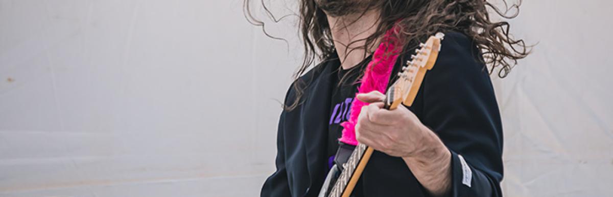 Man with long brown hair and a beard playing a guitar
