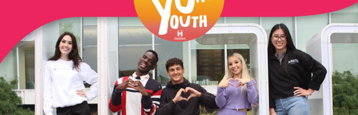 5 young adults sitting on Hamilton Sign at City Hall