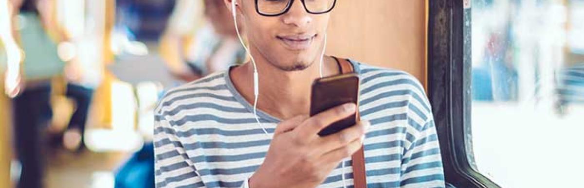 Man sitting on a bus while scrolling phone with headphones on.