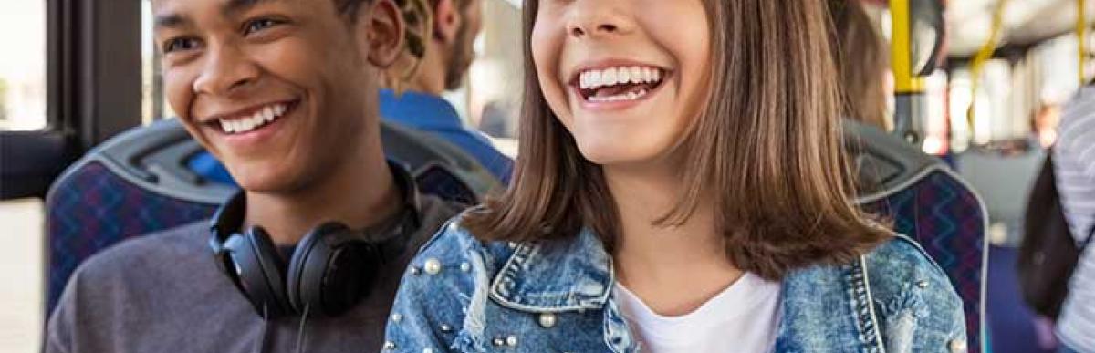 Two teenagers riding the bus smiling