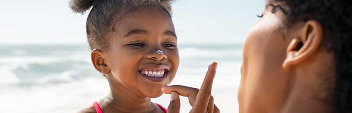 Black mother applying sunscreen to young girl's nose.