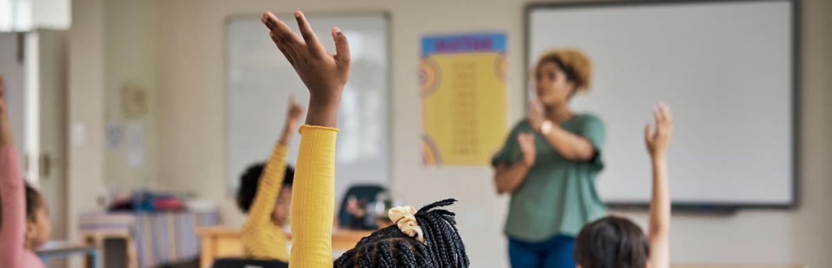 Healthy Schools Certification - students in a classroom with their hands up, a teacher at the front.