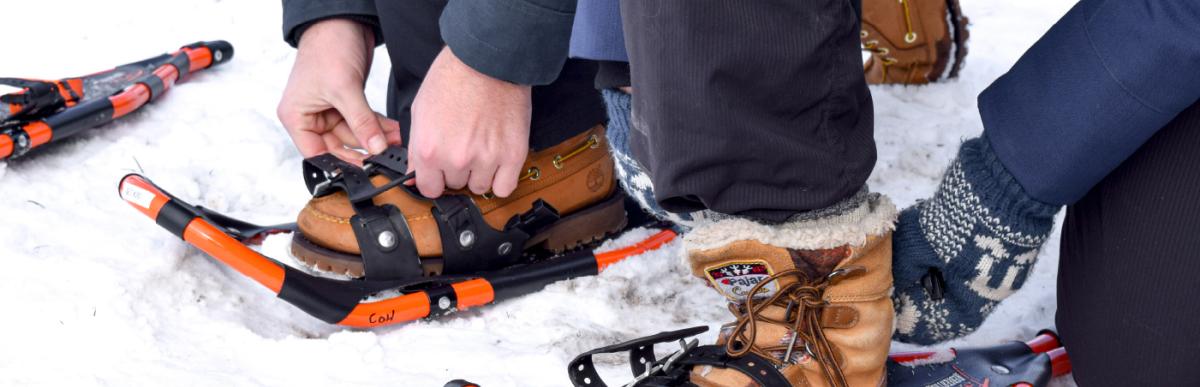 close up on the feet of two people strapping snow shoes on in the snow