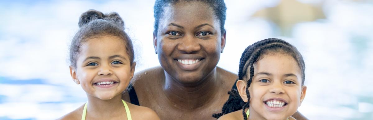 Smiling adult and two smiling children in an indoor swimming pool