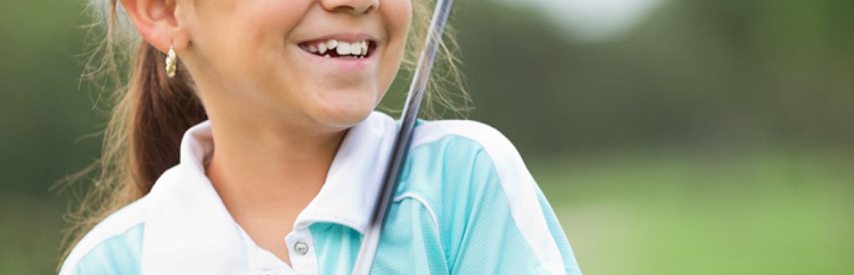 Young girl smiling and looking off-camera while holding a golf club
