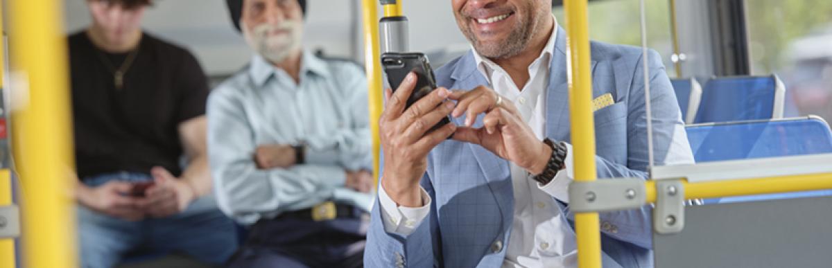 A man in a blue suit jacket smiles at his phone while sitting on an HSR bus