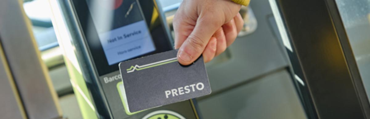 Person's hand holding a PRESTO card up to a card reader on an HSR bus