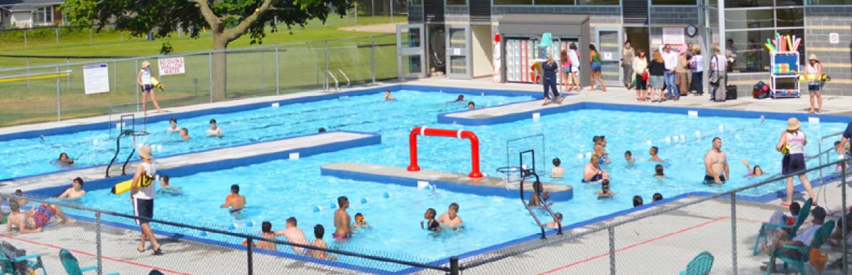 Outdoor public swimming pool full of people of all ages on a bright sunny day