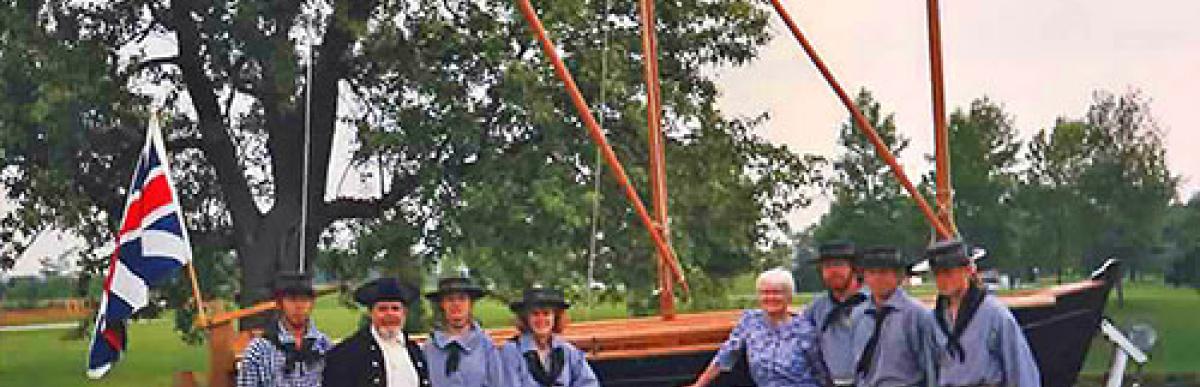 people in period costume standing next to a boat