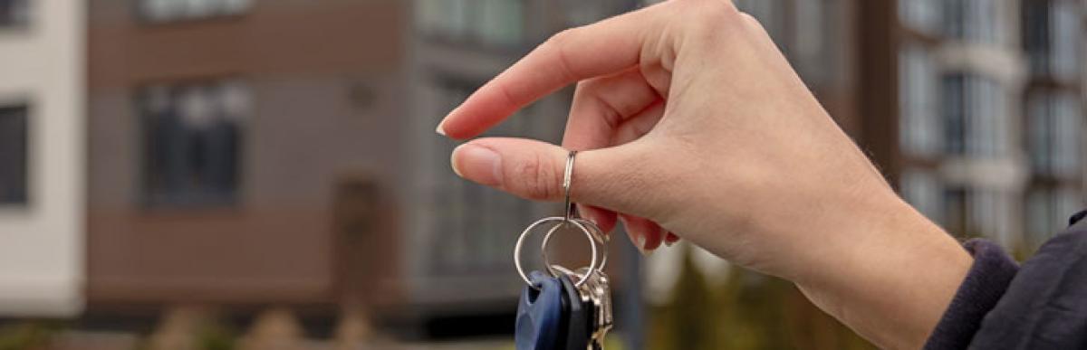 A hand holds a set of keys in the air with an apartment building in the background