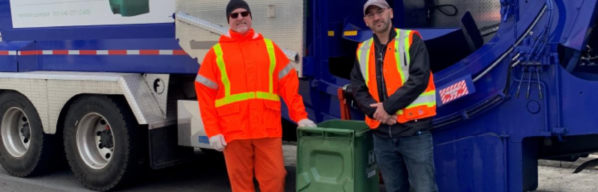 two waste employees standing in front of garbage truck