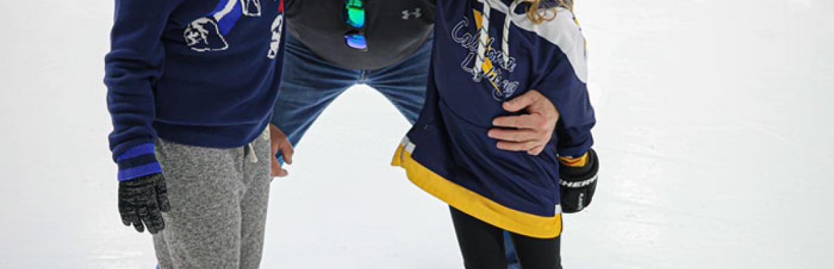 Two children and an adult wearing ice skates in an indoor ice rink