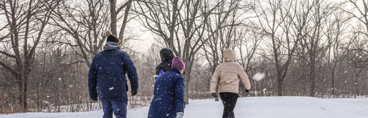 Three people snowshoeing up a snowy hill in a park in winter
