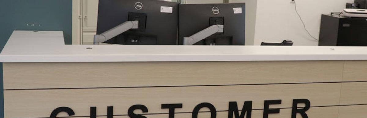 A smiling person stands behind a desk that reads "Customer Service" on the front panel