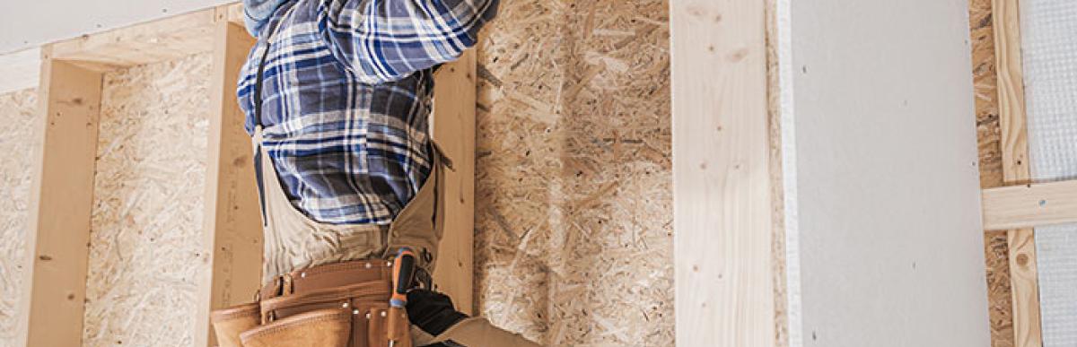 Contractor on ladder drilling screws into drywall on ceiling