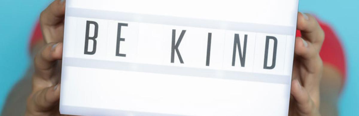 Child holding a light box sign with the letters spelling out "Be Kind"