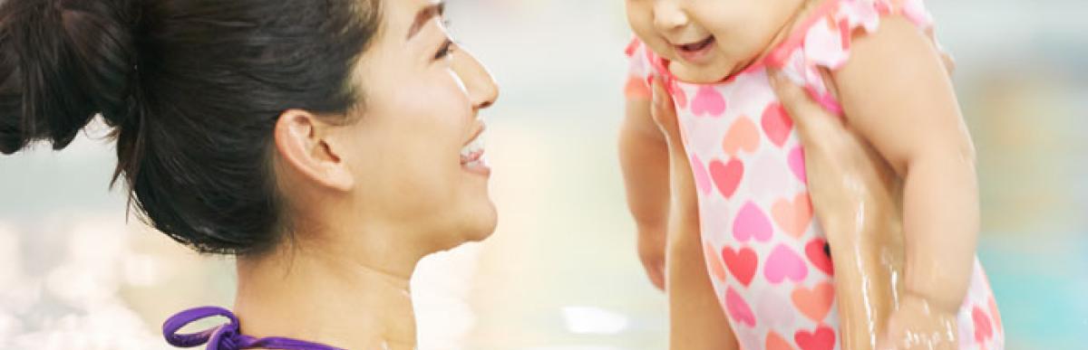 Woman smiling and holding up a baby in a swimming pool