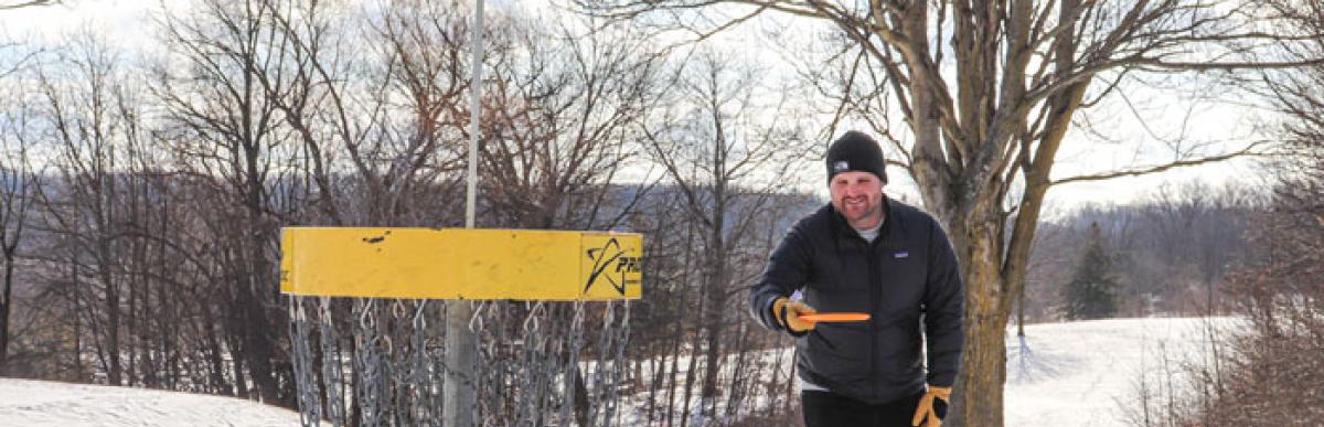 Man in a black winter coat playing disc golf outside on a snowy day