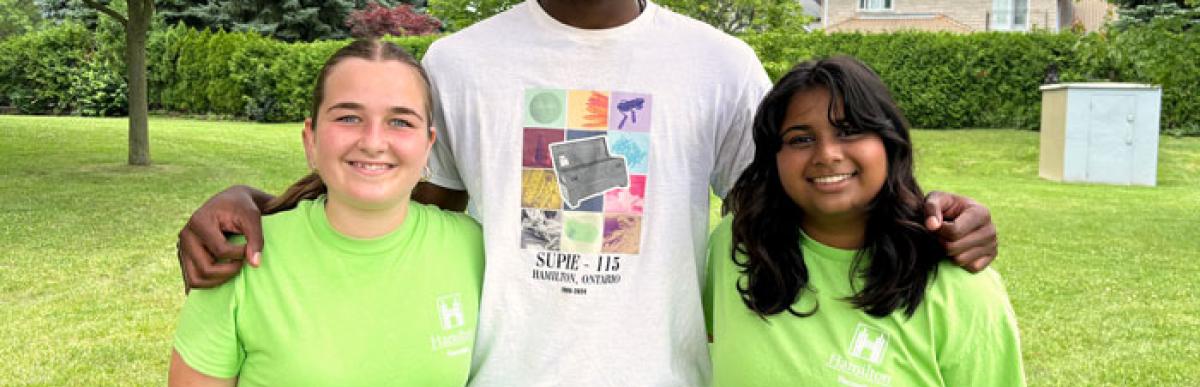 Three summer supie counsellors stand outside in a park, smiling