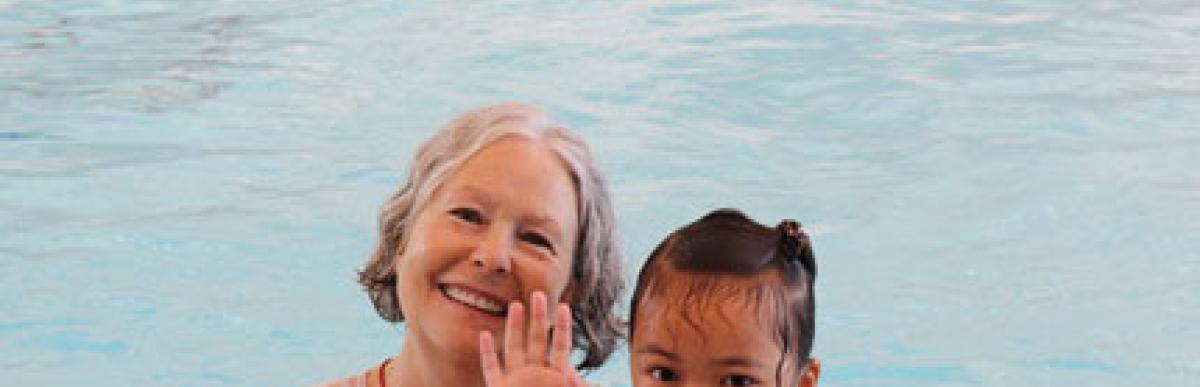 woman and child in an indoor swimming pool, smiling and waving at camera