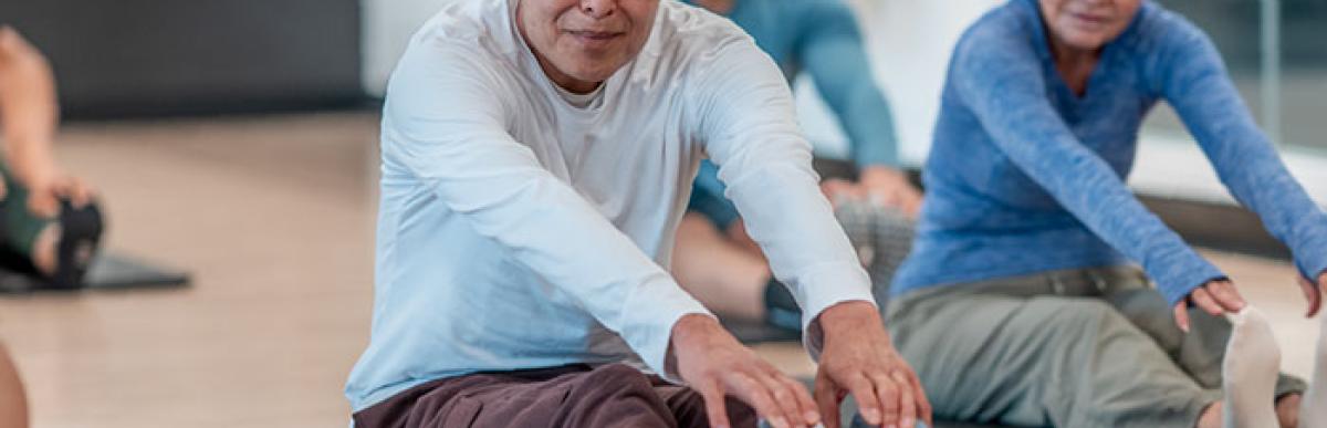 Senior citizens doing stretches on yoga mats in a recreation centre