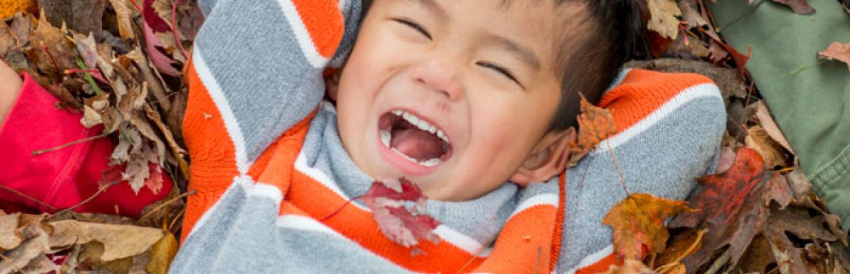 Smiling child lying in a pile of fall leaves