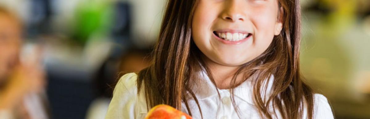 child in a classroom holding a plate of food and smiling