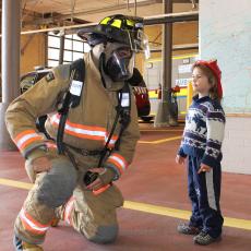 child with a firefighter in full uniform and gear
