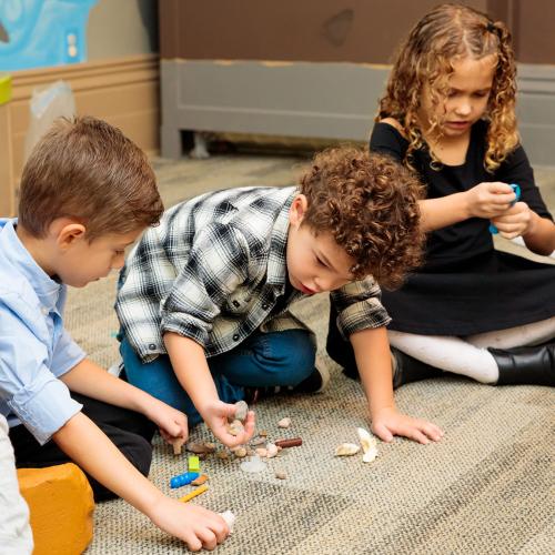 Three kids sitting on the floor and playing with objects