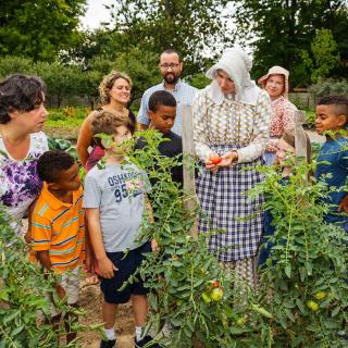 group of children and adults in a garden with a tour guide in period clothing