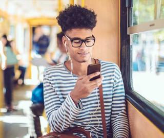 Man sitting on a bus while scrolling phone with headphones on.